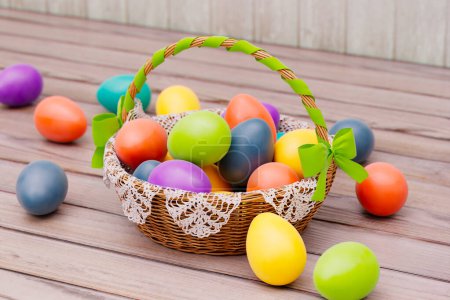 Téléchargez les photos : Un panier de Pâques méticuleusement arrangé rempli d'œufs aux couleurs vives, orné d'un délicat ruban vert, positionné sur une table en bois rustique, invoquant la joie du printemps. - en image libre de droit