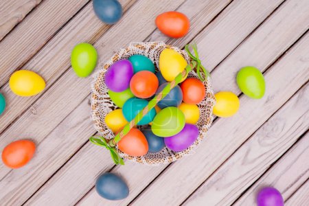 Foto de Exquisita exhibición de huevos de Pascua pintados a mano enclavados en una cesta delicadamente tejida, colocada contra la rica textura de una superficie de madera, evocando la esencia de las festividades de primavera. - Imagen libre de derechos
