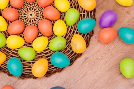 Photo for A picturesque assortment of painted Easter eggs nestled in a traditional wicker basket, contrasted against the rich, textured grain of a rustic wooden table backdrop. - Royalty Free Image