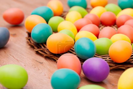 Foto de Una vívida muestra de huevos de Pascua multicolores, tanto en una canasta de mimbre como adornados en una mesa de madera rústica, que encapsula el calor y la alegría de las tradiciones festivas de la primavera.. - Imagen libre de derechos