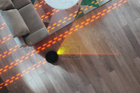 Photo for Smart robot vacuum cleaner efficiently maneuvering under a sofa on a polished hardwood floor, suctioning dust and debris as it leaves a trail on the shiny surface. Ideal for busy households. - Royalty Free Image