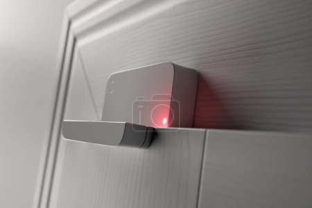 Expertly fitted, high-tech security sensor with a bright red signal light prominently displayed on a white door, embodying cutting-edge home safety and smart monitoring in a domestic setting.