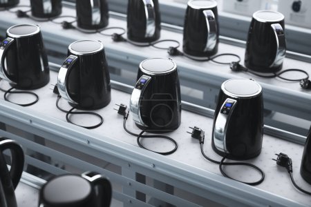 Automated assembly line featuring multiple black electric kettles with touch interfaces, emblematic of contemporary kitchen appliances and industrial manufacturing efficiency.
