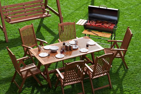 Téléchargez les photos : Un arrangement de salle à manger en plein air accueillant avec une table et des chaises rustiques en bois attend les invités, tandis que les viandes grésillent sur un barbecue à proximité au milieu d'un jardin verdoyant. - en image libre de droit