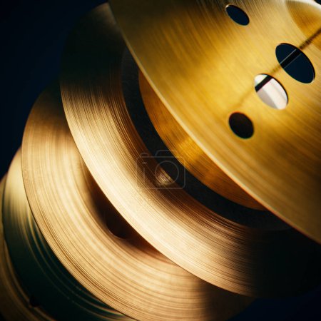 Foto de Macro shot captura los intrincados detalles de los relucientes carretes de metal dorado con agujeros de corte preciso, acentuados por una llamativa iluminación de contraste sobre un fondo oscuro y silencioso. - Imagen libre de derechos