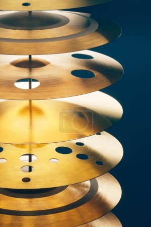 Téléchargez les photos : Vue rapprochée d'un arrangement soigneusement empilé de cymbales dorées présentant des découpes circulaires, sur fond bleu profond contrasté pour une composition abstraite frappante. - en image libre de droit