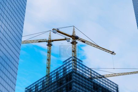 Photo for Majestic tower cranes dominate the emerging silhouette of a new building amidst the hustle of city life, with the azure sky backdrop highlighting the modern urban growth - Royalty Free Image