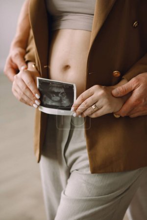 Mujer embarazada con su marido sosteniendo una foto de ultrasonido cerca del vientre embarazada. Concepto familiar. El concepto de maternidad feliz y paternidad
