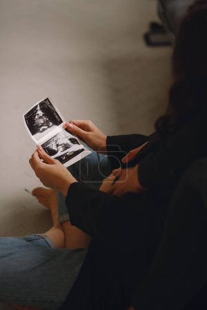 Pregnant woman in black jacket and blue jeans and her husband looking at the ultrasound picture. Love concept. Family concept. The concept of happy parenthood