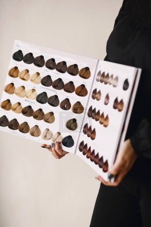 Close up photo of hair stylist with hair samples of different colors. Hairdresser looks at hair color samples on palette swatch book. Copy space for text 