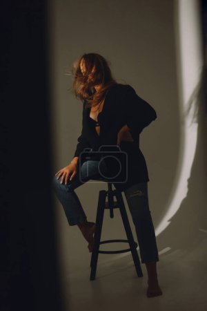 Foto de Young woman in black bra, jacket and jeans posing on a cyclorama with blowing hair. Beaty and fashion - Imagen libre de derechos
