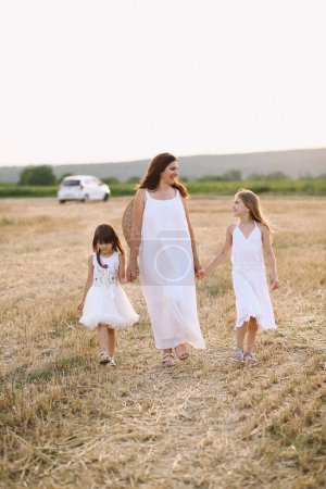Mère et ses deux filles en robes blanches d'été marchant dans les champs. Joyeux concept de maternité. Concept de famille. Séance photo d'été. Temps des fêtes. Saison estivale