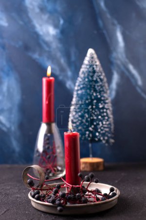 Photo for Christmas decorations. Red burning candle in rustic holder, wid blue berries and blue decorative tree against blue  textured background. Scandinavian minimalistic style. Still life. - Royalty Free Image