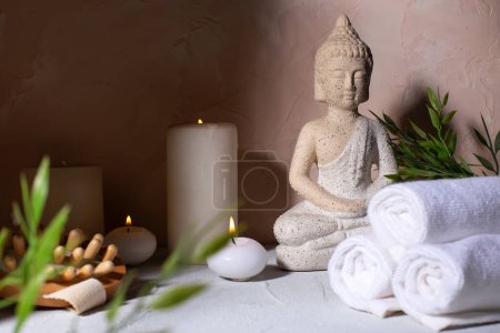 Spa beauty wellness concept with statue of Buddha with burning candles for spa time.  Massage brush, towels, green plants. Spa concept. 