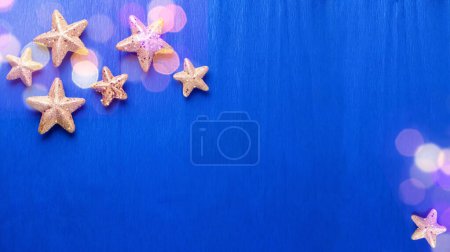 Foto de Postal de grandes y pequeñas estrellas decorativas doradas y luz bokeh sobre fondo texturizado de papel eléctrico. Vista superior. Navidad, concepto de vacaciones de Año Nuevo. Lugar para el texto. - Imagen libre de derechos