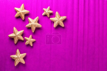 Foto de Postal con grandes y pequeñas estrellas decorativas doradas sobre fondo texturizado de papel rosa brillante. Vista superior. Navidad, concepto de vacaciones de Año Nuevo. Lugar para el texto. - Imagen libre de derechos