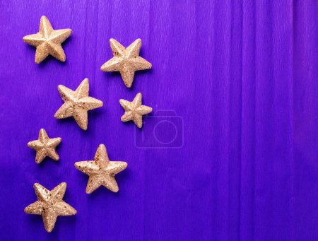 Téléchargez les photos : Carte postale avec de grandes et petites étoiles décoratives dorées sur fond texturé en papier violet. Vue de dessus. Noël, Nouvel An concept de vacances. Place pour le texte. - en image libre de droit