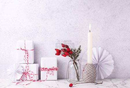 Photo for Postcard with  wrapped boxes with presents, briar berries in bottle, burning candle against textured  wall. Scandinavian style. Place for text. - Royalty Free Image