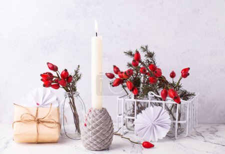 Photo for Postcard with  burning candle, wrapped box with present, briar berries in bottle, against textured  wall. Scandinavian style. Place for text. - Royalty Free Image
