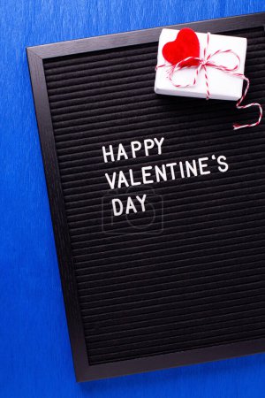 Photo for St. Valentines day card. Letterboard with congratulation phrase  and box with present and hearts  oh bright blue paper textured background. Top view. - Royalty Free Image