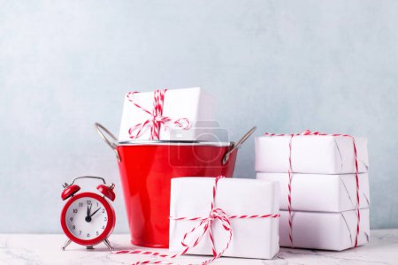 Photo for Composition with  wrapped boxes with presents in red bucket and red clock against  blue textured  wall. Scandinavian style. Place for text. - Royalty Free Image