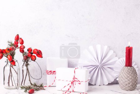 Photo for Wrapped boxes with presents, briar berries in bottle, paper, rosettes, burning red candle against textured  wall. Scandinavian style. Place for text. - Royalty Free Image
