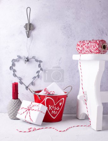 Photo for Postcard with  wrapped presents in bucket, heart, red candle  against  grey  textured  wall.  St. Valentines day postcard. Place for text. - Royalty Free Image