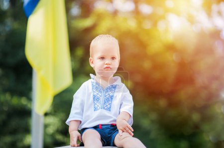 Téléchargez les photos : Tout-petit garçon en ukrainien vyshyvanka sur fond de drapeau jaune-bleu ukrainien en été. - en image libre de droit