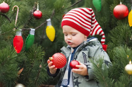 Foto de Lindo niño sosteniendo la bola de Navidad en el patio trasero decorado de cerca y espacio de copia. Feliz celebración.. - Imagen libre de derechos