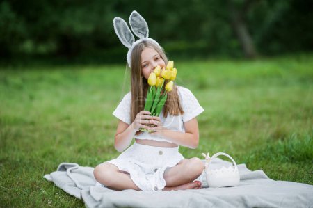 Foto de Feliz Pascua. Retrato de niña con tulipanes amarillos en la naturaleza de cerca. Chica con orejas de conejo - Imagen libre de derechos