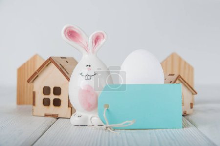 Foto de Feliz tarjeta de felicitación de Pascua. Casa de madera en miniatura. Conejos, huevos de colores, flores de primavera con etiqueta de texto. - Imagen libre de derechos