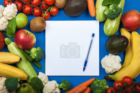 Téléchargez les photos : Beaucoup de variété de légumes et de fruits frais sur fond bleu avec un espace de copie de bloc-notes blanc. Alimentation saine, concept de régime alimentaire - en image libre de droit