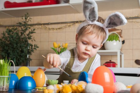 Téléchargez les photos : Petit garçon peignant Oeuf de Pâques gros plan. Traditions de Pâques et divertissement avec les enfants à la maison. - en image libre de droit