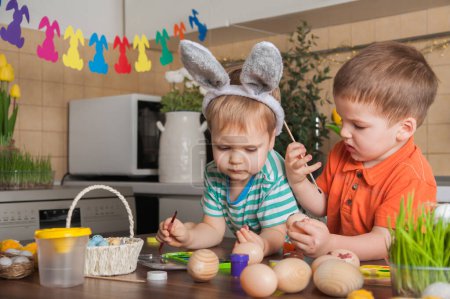 Téléchargez les photos : Des enfants peignent des œufs de Pâques. Traditions de Pâques, plaisir avec les tout-petits - en image libre de droit