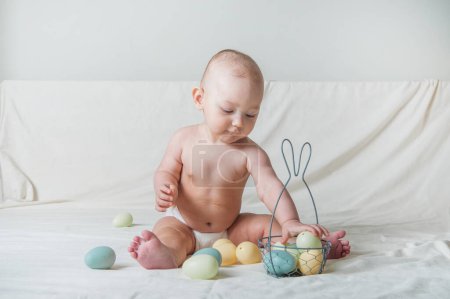 Foto de Niña de 1 año en la cama con cesta y huevos de Pascua. Caza de huevos, actividad infantil. - Imagen libre de derechos