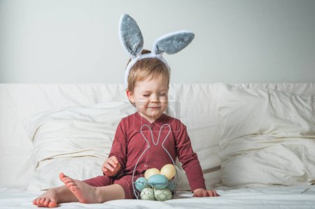 Photo for Toddler boy on bed with basket and Easter eggs. Egg hunting, kids activity. - Royalty Free Image