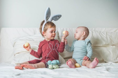 Téléchargez les photos : Enfants à la maison avec panier de Pâques sur le lit. Frère et sœur trouvent des œufs de Pâques. - en image libre de droit
