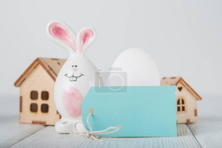 Téléchargez les photos : Bonne carte de vœux de Pâques. Maison en bois miniature. Lapins, oeufs colorés, fleurs de printemps avec étiquette pour le texte. - en image libre de droit