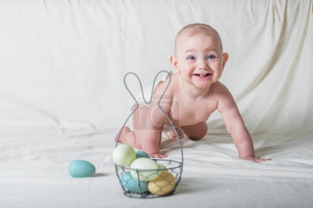 Photo for Baby girl 1 year old on bed with basket and Easter eggs. Egg hunting, kids activity. - Royalty Free Image