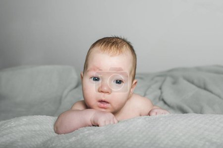 A baby with a gentle expression lies comfortably on a textured blanket, looking towards the camera with wide-eyed curiosity. The soft lighting enhances the calming atmosphere, highlighting the babys