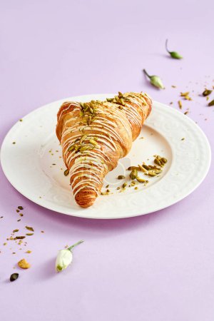 Foto de Croissant with pistachio cream and sprinkle of nuts on a white plate on a pink background - Imagen libre de derechos