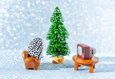 Photo for Creative Christmas brainwashing concept: anatomical copy of a human brain watching TV sitting in a chair by a new year tree. - Royalty Free Image