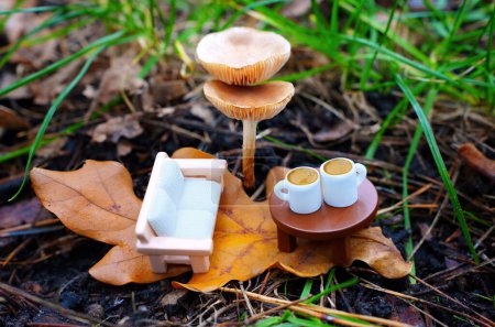 Miniatur-Sofa und Kaffeetassen auf einem Spielzeugtisch, eingebettet in die aufragenden Pilze im Wald. Beruhigende Flucht aus dem Alltag.