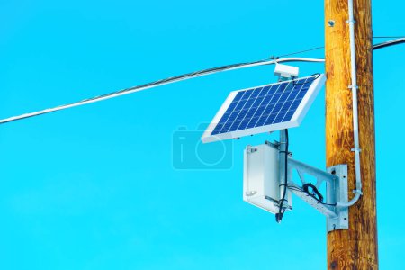 Photo for Solar panel and auxiliary equipment mounted on a wooden pole of an electric power line against a vibrant blue sky. - Royalty Free Image