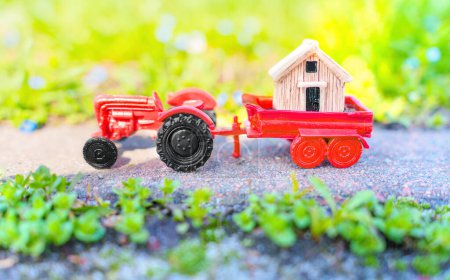 Téléchargez les photos : Petite maison en bois placée sur une remorque tracteur jouet, garée sur une route pavée dans le jardin. Jardin hangar concept de livraison. - en image libre de droit