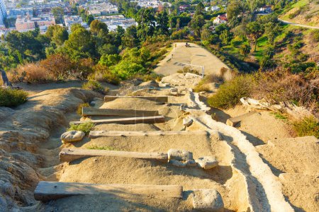 Wooden steps carved into the rocks lead to a vista point at Runyon Canyon Park in California, offering a stunning view of the city below and the surrounding landscape.