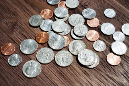 Monedas estadounidenses iluminadas por el sol colocadas en una mesa de madera oscura que capturan la esencia de las transacciones financieras, los ahorros o los conceptos de inversión.
