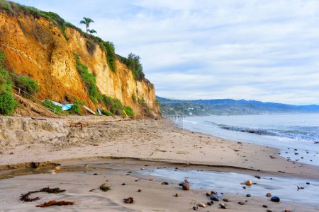 A beautiful coastal landscape with a rocky cliff, sandy shore and ocean view in Malibu, California.