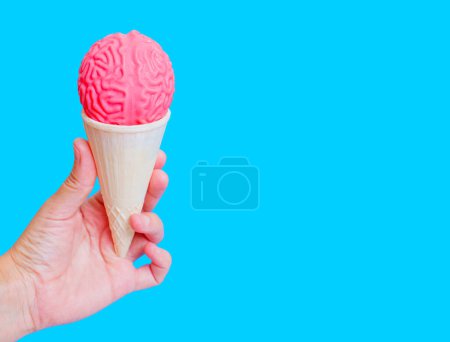 Photo for Hand holding an ice cream cone topped with a delicious scoop of brain-shaped model isolated on blue background. Creative brainy enjoyment concept. - Royalty Free Image