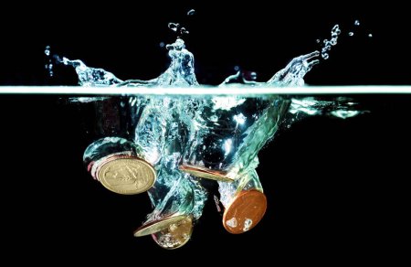 Foto de Primer plano de un grupo de monedas arrojadas en el agua con salpicaduras en negro. Concepto relacionado con el blanqueo de capitales. - Imagen libre de derechos